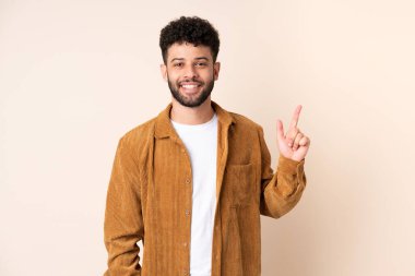 Bej arka planda izole genç Faslı adam en iyinin işareti olarak parmağını kaldırıyor ve gösteriyor.