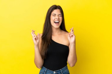 Young Brazilian woman isolated on yellow background with fingers crossing