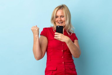 Middle age woman isolated on blue background with phone in victory position