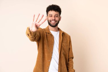 Bej arka planda izole edilmiş genç Faslı adam mutlu ve parmakları olan dört kişi sayıyor.
