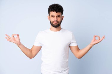 Genç Faslı adam mavi arka planda Zen pozunda izole edilmiş.