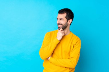 İzole edilmiş mavi arka planda genç bir beyaz adam yan tarafa bakıyor.