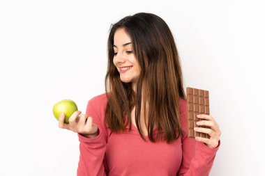 Pembe arka planda izole edilmiş beyaz bir kadın bir elinde çikolata tableti, diğerinde elma alıyor.