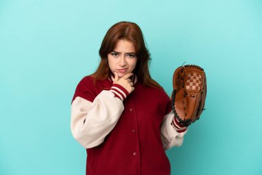 Young redhead woman playing baseball isolated on blue background thinking