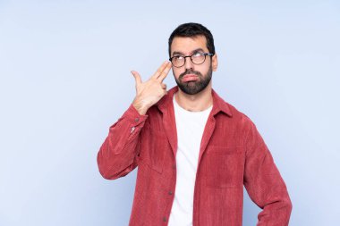 Young caucasian man wearing corduroy jacket over blue background with problems making suicide gesture