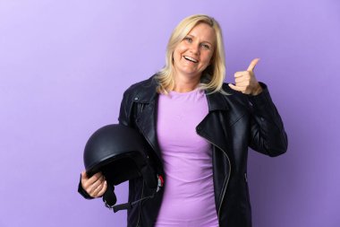 Middle age woman holding a motorcycle helmet isolated on purple background making phone gesture. Call me back sign