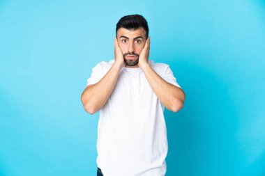 İzole edilmiş mavi arka planı olan beyaz bir adam hayal kırıklığına uğramış ve kulaklarını kapatmış.