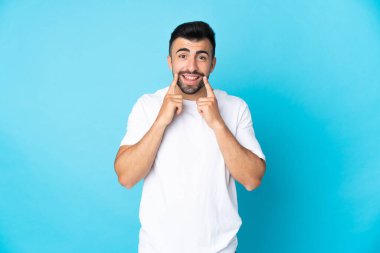 İzole edilmiş mavi arka planı olan beyaz bir adam mutlu ve hoş bir ifadeyle gülümsüyor.