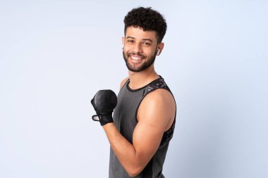 Faslı genç adam mavi arka planda izole edilmiş halter yapıyor.