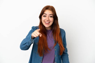 Beyaz arka planda izole edilmiş genç kızıl saçlı kadın şaşırmış ve ön tarafı işaret ediyor.