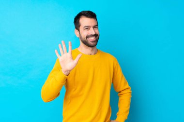 İzole edilmiş mavi arka planda genç beyaz adam parmaklarıyla beşi sayıyor.