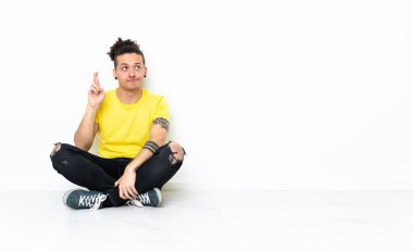 Caucasian man sitting on the floor with fingers crossing and wishing the best
