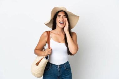 Young Brazilian woman with Pamela holding a beach bag isolated on white background shouting with mouth wide open