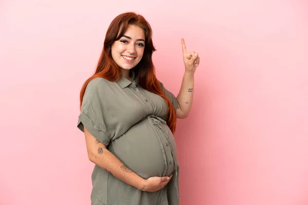 若いですRedhead Caucasian女性隔離上のピンクの背景妊娠中や指摘 — ストック写真