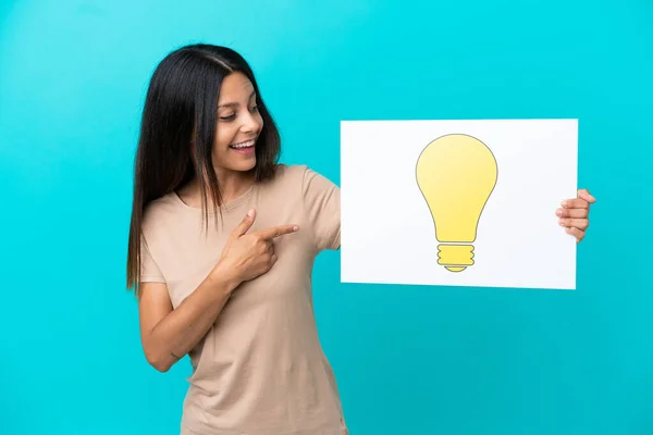 Young Woman Isolated Background Holding Placard Bulb Icon Pointing — Stock Photo, Image