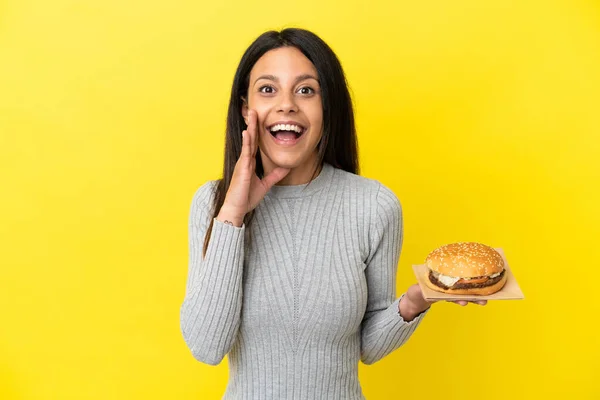 Young Caucasian Woman Holding Burger Isolated Yellow Background Surprise Shocked — Stock Photo, Image
