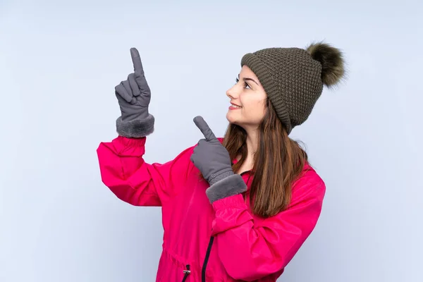 年轻姑娘戴着冬帽 蓝色背景 用食指指尖 这真是个好主意 — 图库照片