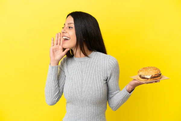 Young Caucasian Woman Holding Burger Isolated Yellow Background Shouting Mouth — Stock Photo, Image