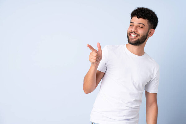 Молодой марокканский человек выделяется на синем фоне, указывая пальцем в сторону и представляя продукт