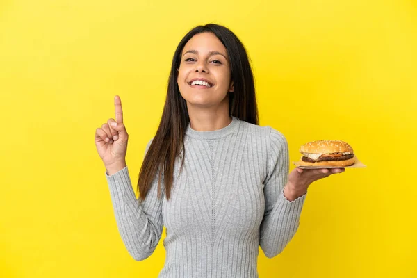 Young Caucasian Woman Holding Burger Isolated Yellow Background Showing Lifting — Stock Photo, Image