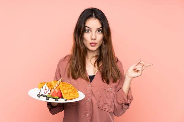 Young Caucasian Woman Holding Waffles Isolated Pink Background Surprised Pointing — Stock Fotó