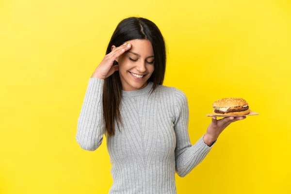Young Caucasian Woman Holding Burger Isolated Yellow Background Laughing — Stock Photo, Image