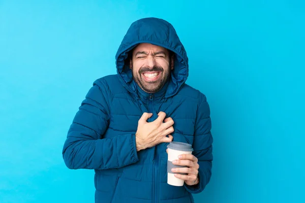 stock image Man wearing winter jacket and holding a takeaway coffee over isolated blue background having a pain in the heart