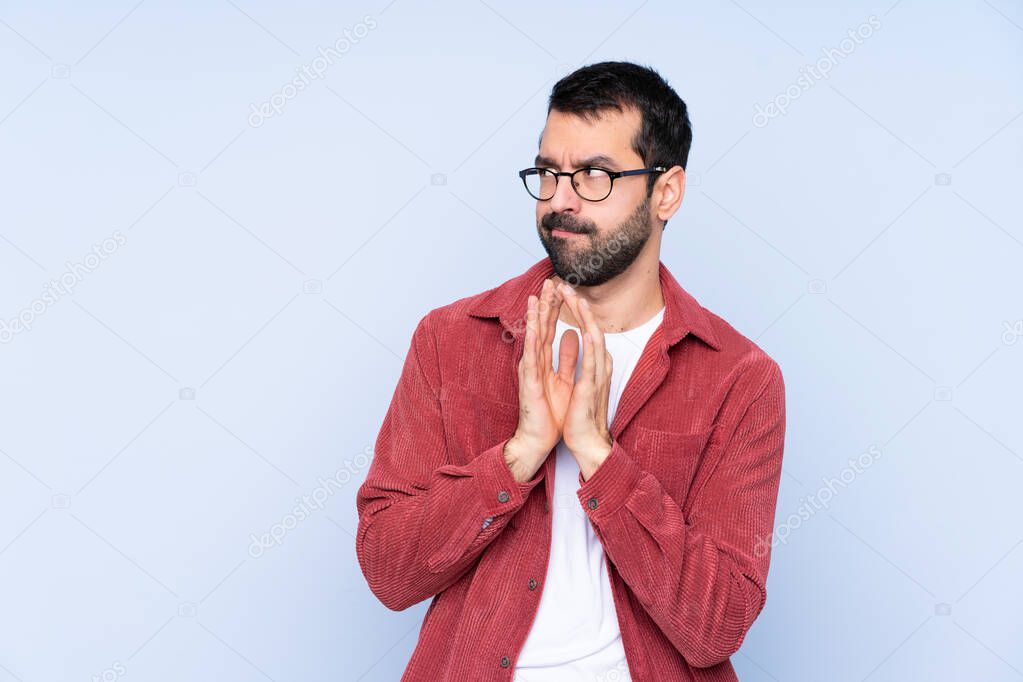 Young caucasian man wearing corduroy jacket over blue background scheming something