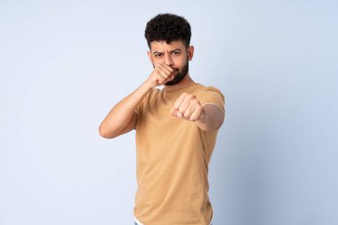 Young Moroccan man isolated on blue background with fighting gesture