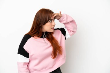 Genç kızıl saçlı kadın beyaz arka planda izole edilmiş. Sürpriz bir ifadeyle yan tarafa bakıyor.