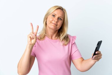 Middle age using mobile phone isolated on white background smiling and showing victory sign