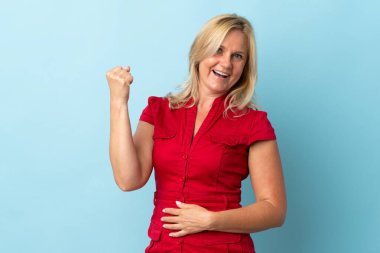 Mavi arka planda izole edilmiş orta yaşlı kadın zaferi kutluyor.
