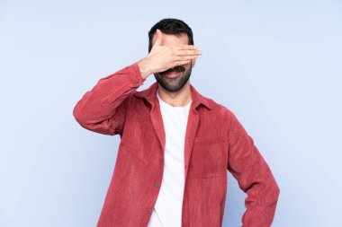 Young caucasian man wearing corduroy jacket over blue background covering eyes by hands. Do not want to see something