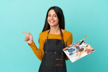 Kafkasyalı genç bir kadın mavi arka planda izole edilmiş bir palet tutuyor.