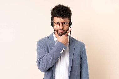 Telemarketer Moroccan man working with a headset isolated on beige background thinking