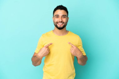 Genç Arap adam mavi arka planda yalıtılmış ve şaşırmış bir yüz ifadesi var.