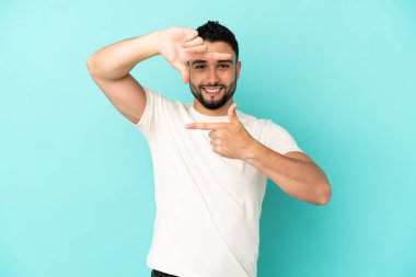 Genç Arap adam mavi arka planda izole edilmiş, odaklanan yüz. Çerçeve sembolü