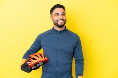 Genç bisikletçi Arap adam sarı arka planda izole edilmiş bir şekilde yukarı bakarken bir fikir düşünüyor.