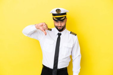 Arap uçak pilotu, sarı arka planda izole edilmiş, negatif ifadeyle baş parmağını gösteriyor.