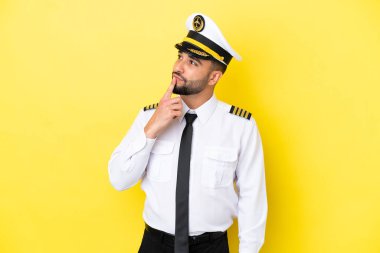 Arap uçak pilotu, sarı arka planda izole edilmiş, yukarı bakarken şüpheleri var.