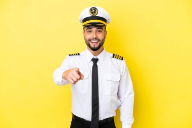 Arap uçak pilotu sarı arka planda izole edilmiş şaşırmış ve ön tarafı işaret ediyor.