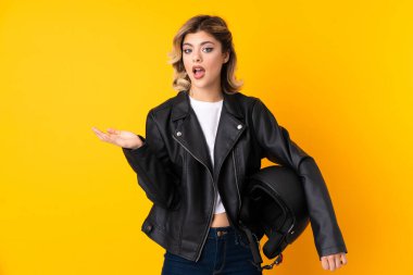 Elinde motosiklet kaskı olan genç bir kadın sarı arka planda izole edilmiş.