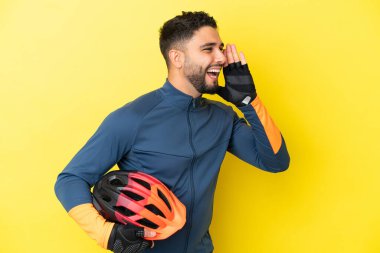 Sarı arka planda izole edilmiş genç bisikletçi ağzı sonuna kadar açık bağırıyor.