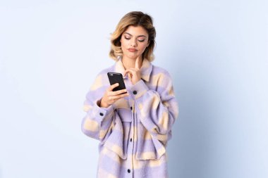 Genç Rus kadın mavi arka planda izole edilmiş düşünüyor ve bir mesaj gönderiyor.