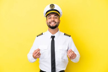 Arap uçak pilotu sarı arka planda izole edilmiş para hareketi yapıyor.