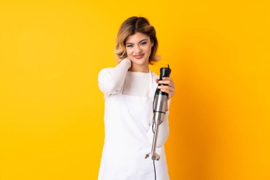 Sarı arka planda izole edilmiş el blenderi kullanan kız gülüyor.