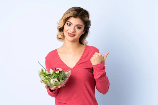Mulher Adolescente Com Salada Isolada Fundo Azul Apontando Para Lado — Fotografia de Stock