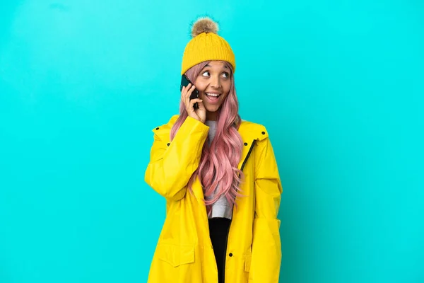穿着防雨外套 背景为蓝色的年轻女子 带着粉红头发 与手机交谈 — 图库照片