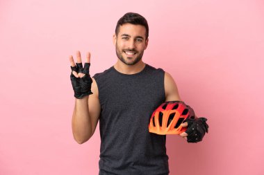 Pembe arka planda izole edilmiş genç bisikletçi mutlu ve parmaklarıyla üçe kadar sayıyor