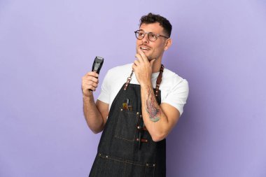 Mor arka planda izole edilmiş önlüklü beyaz bir adam gülümserken yukarı bakıyor.